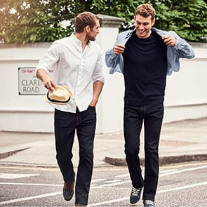 Two men wearing jeans walking along a street