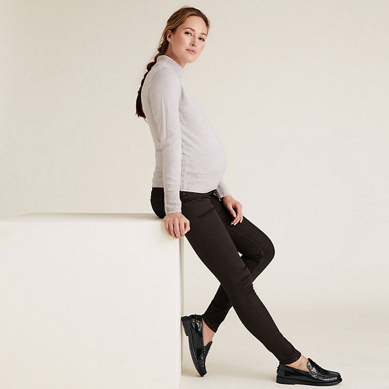 Woman wearing cream roll-neck maternity top, black maternity jeans and black loafers