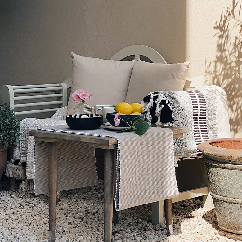 Outdoor sofa, neutral cushions and throws and table set up for breakfast