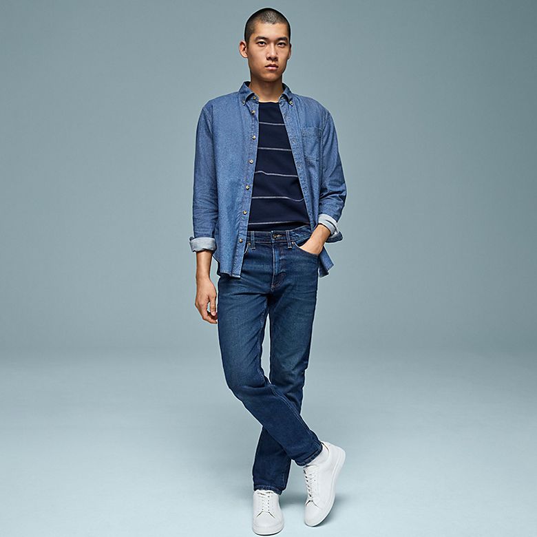 Man wearing medium blue skinny-fit jeans, a navy striped t-shirt and a denim shacket. Shop men’s skinny-fit jeans
