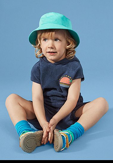Boy wearing navy T-shirt and shorts and bright blue sun hat, socks and sandals