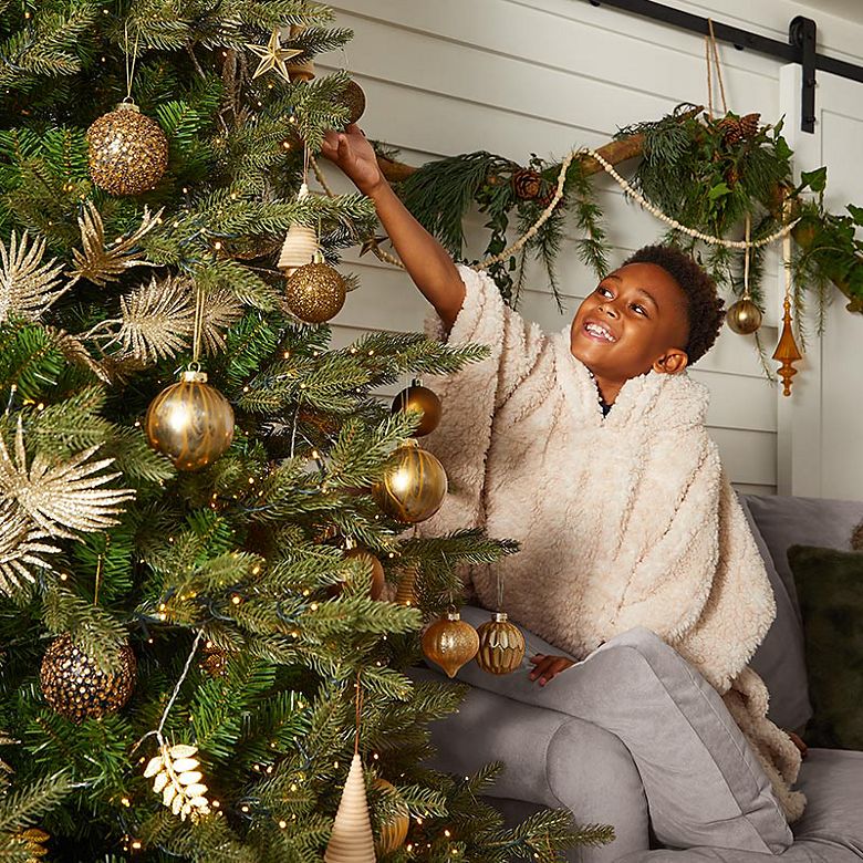 Little boy decorating a Christmas tree with gold decorations. Shop Christmas baubles 