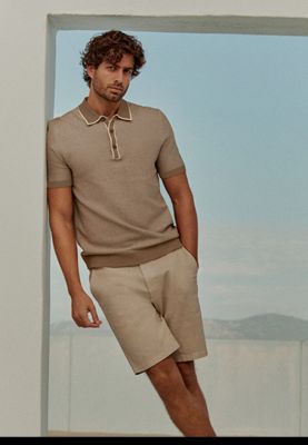Man wearing beige polo-shirt and beige chino shorts. Shop polo shirts