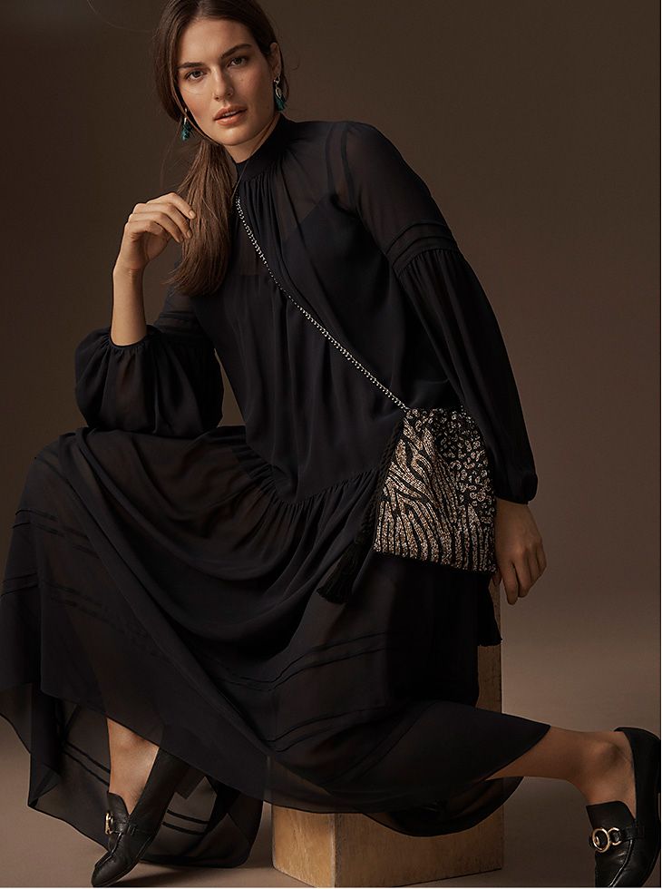 Model wears a long black chiffon dress with a beaded evening bag and black buckled loafers