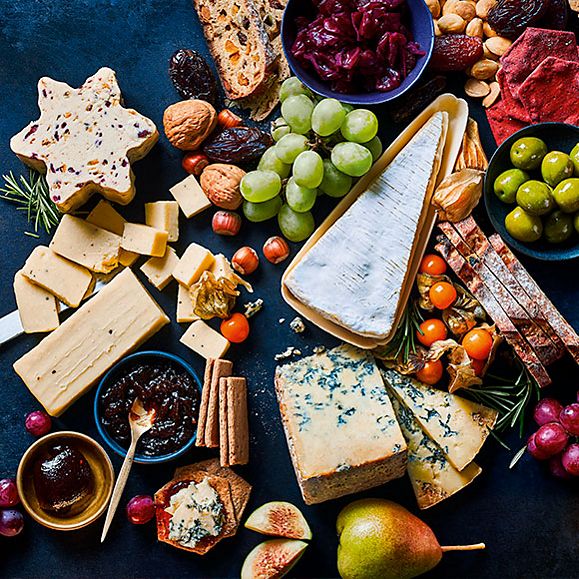 Busy cheeseboard filled with Christmas cheese and grapes and crackers