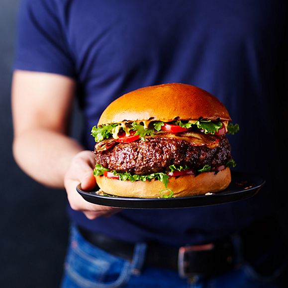  A man holding a daddy of all burger in a giant brioche bun with lettuce and tomato