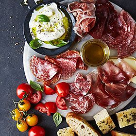 A board filled with cured meats, bread, tomatoes and mozzarella