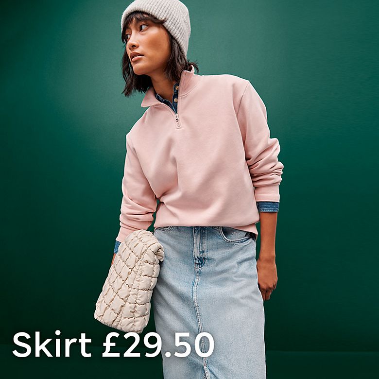 Woman wearing pink zip top, blue denim skirt and a pink knitted hat. Shop women’s skirts  