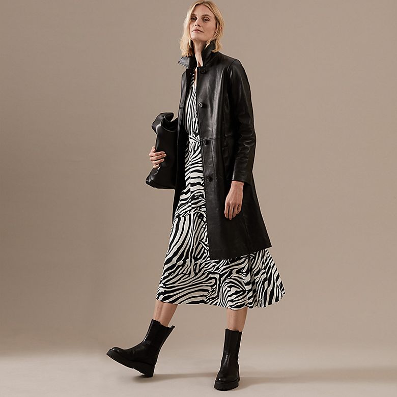 Woman wearing black and white zebra-print dress, black leather coat, black bag and black boots. Hire now