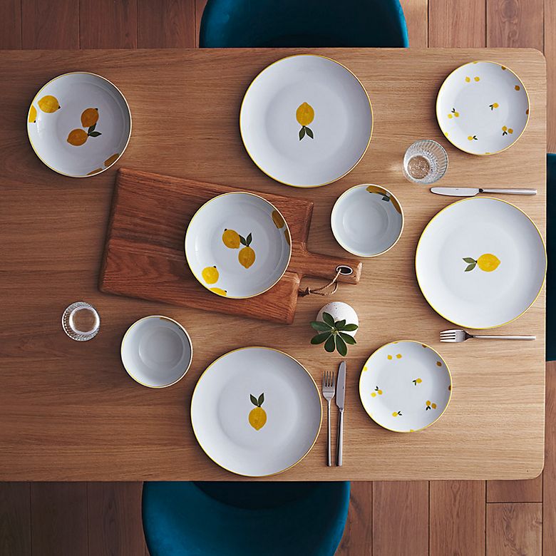 Wooden table set with lemon-design crockery, wooden board, silver cutlery, water glasses and vase