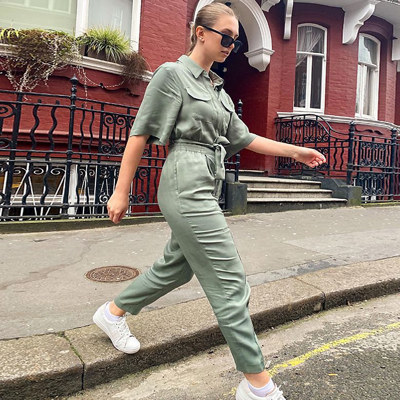 Woman wearing khaki jumpsuit and white trainers