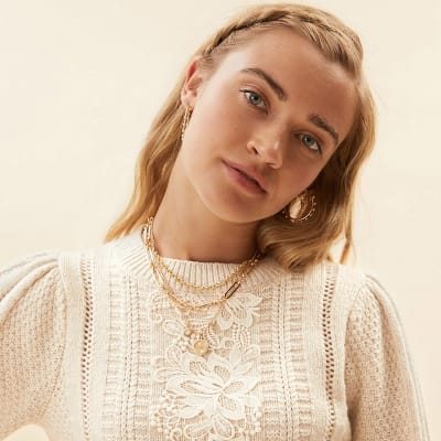 Woman wearing lots of gold jewellery and a cream cable knit jumper