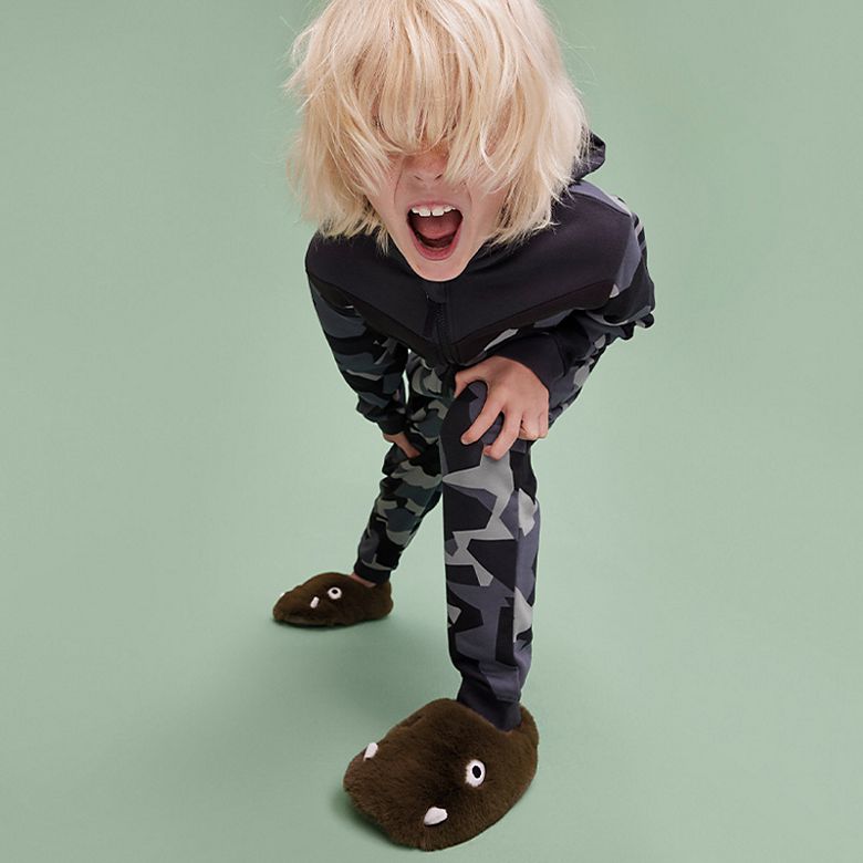Child wearing camo-print loungewear and dinosaur slippers