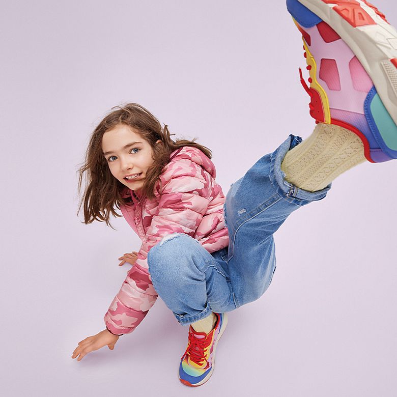 Child wearing jeans, pink puffer coat and bright rainbow trainers