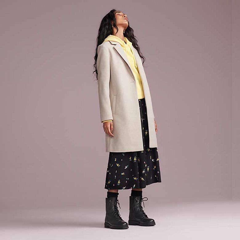 Woman wearing beige coat, yellow hoodie, floral midi dress and lace-up boots