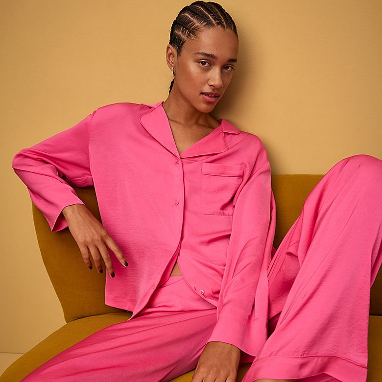 Woman wearing pink satin pyjama set. Shop women’s nightwear 