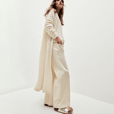 Woman wearing long cream cardigan, cream trouser and metallic sandals. Shop women’s new-in 