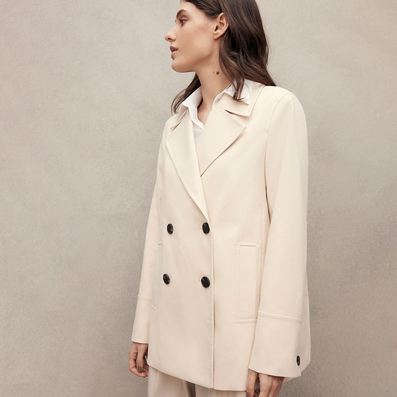 Woman wearing a cream cotton double-breasted jacket. Shop all coats and jackets 