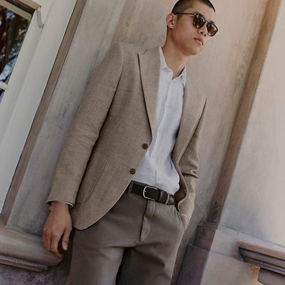 Man wearing sunglasses, light brown blazer, white shirt and light brown trousers. Shop men’s summer workwear 