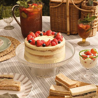Outdoor table with cake, finger sandwiches and a jug of fruit cocktail. Shop party food 
