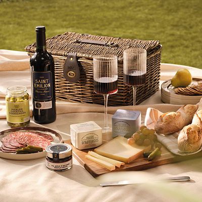 Wicker hamper with a selection of French food and wine on an outdoor table. Shop food hampers
