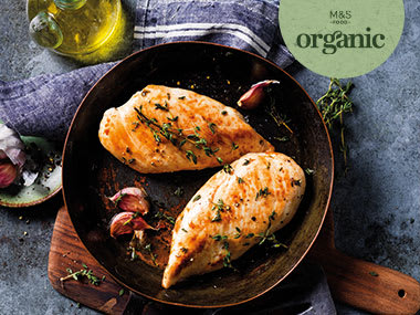 A cooked organic chicken surrounded by roasted vegetables