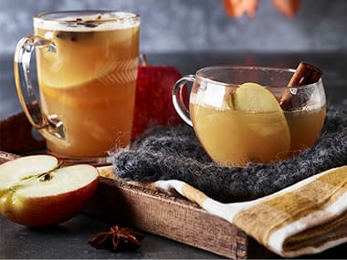 	 A jug and glass of warm apple cider with apples and a sprig of cinnamon