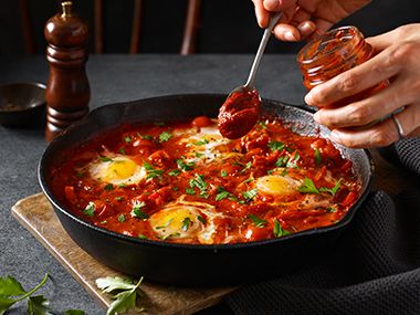 A tray of shakshuka with a person spooning in M&S smoked tomato paste