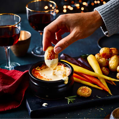 A man dunking a roast potato into a cheese fondue