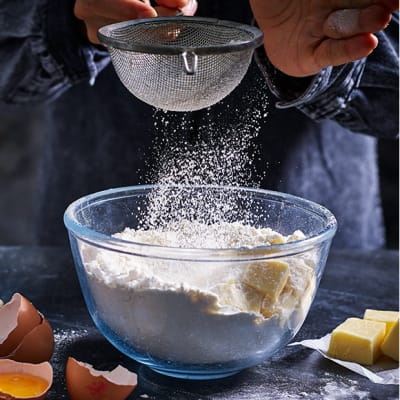 Flour being sieved into a bowl of butter and eggs 