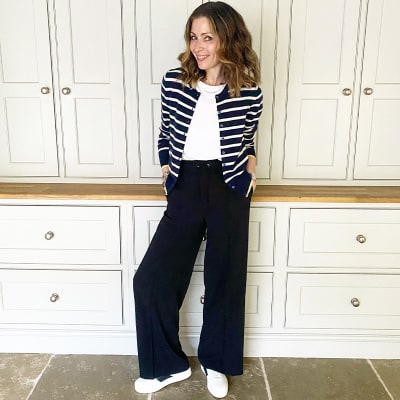 Woman wearing Breton cardigan, white tank, slouchy black trousers and white trainers 
