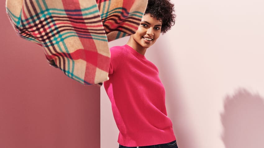 Woman wearing pink cashmere jumper and holding patterned cashmere scarf