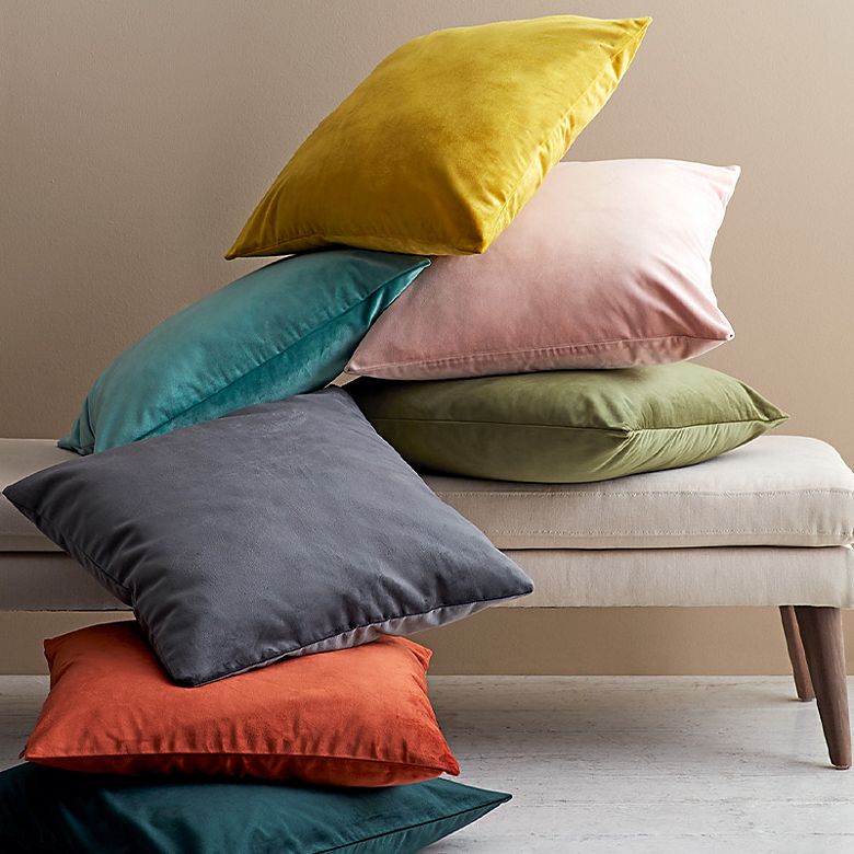 Velvet cushions in various colours stacked on and next to an ottoman