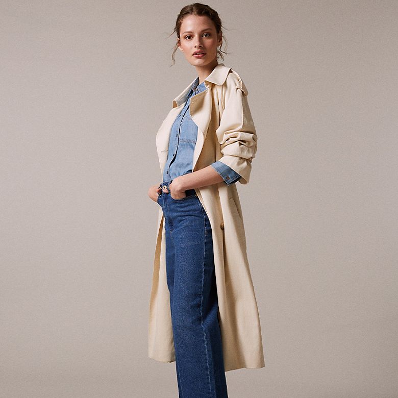 Woman wearing a fluid cream trench over a denim shirt and wide-leg jeans