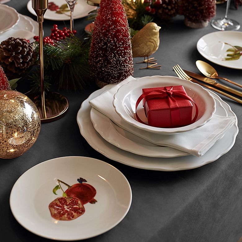 Christmas table set with white crockery, with red tree decorations and candles in gold holders
