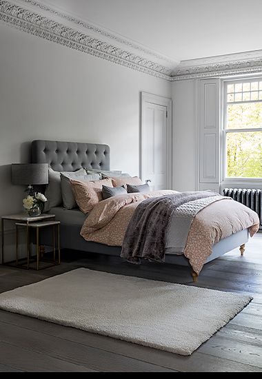 Bedroom with bed made up in pink and grey bedding and rug on the floor