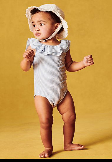 Baby boy wearing light blue striped frill-neck swimsuit and white sun hat 