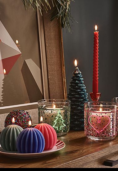 A selection of festive candles on a sideboard. Shop candles 