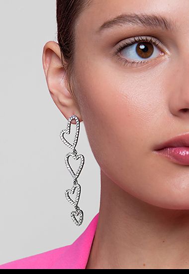 Woman wearing heart-shaped diamante drop earrings. Shop now