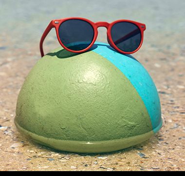 Kid’s red round sunglasses balancing on a beach ball in the sea. Shop kids’ sunglasses.