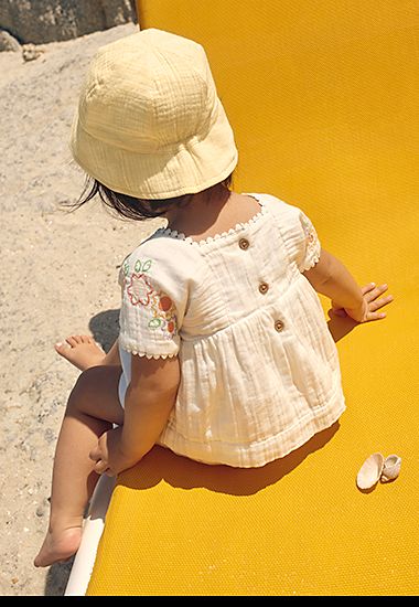 Girl wearing yellow sun hat and cotton dress with button detail. Shop kids’ sun hats. 