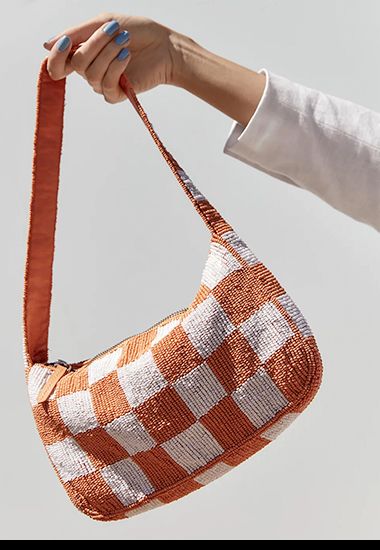 Woman holding Y2K style orange and white beaded checked baguette bag. Shop now. 