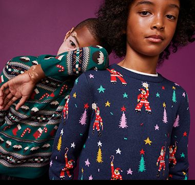 Two children wearing Christmas jumpers. Shop kids’ knitwear