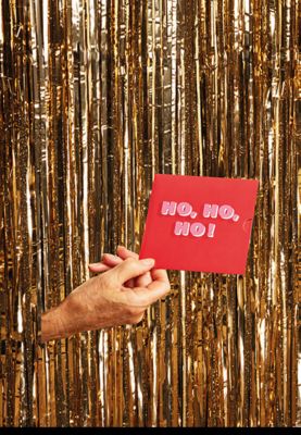 Hand poking through glitter curtain holding red ‘Ho, Ho, Ho!’ design M&S gift card. Shop gift cards