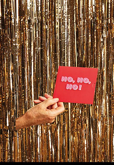 Hand poking through glitter curtain holding red ‘Ho, Ho, Ho!’ design M&S gift card. Shop gift cards