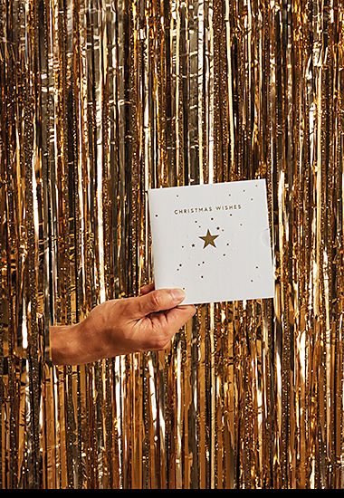 Hand poking through glitter curtain holding M&S gift card. Shop gift cards