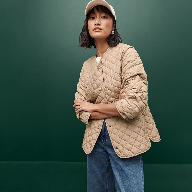 Woman wearing a pink quilted jacket and jeans. Shop women’s coats and jackets 