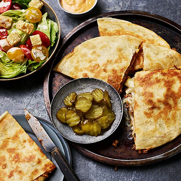 Cheeseburger quesadillas cut into quarters with bowl of pickle coins