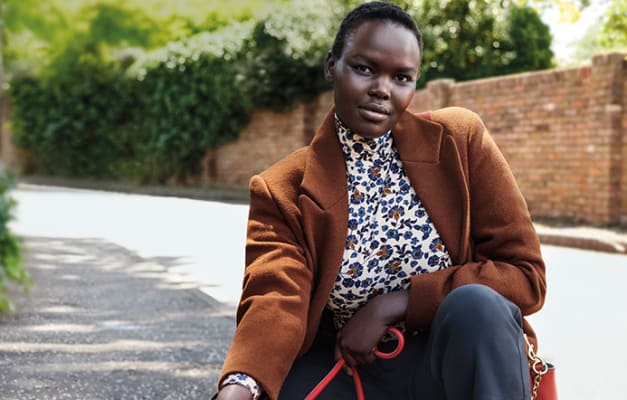 Woman wearing a tan overcoat and cream floral polo neck