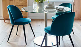 Teal velvet dining chairs around a glass and metal round dining table